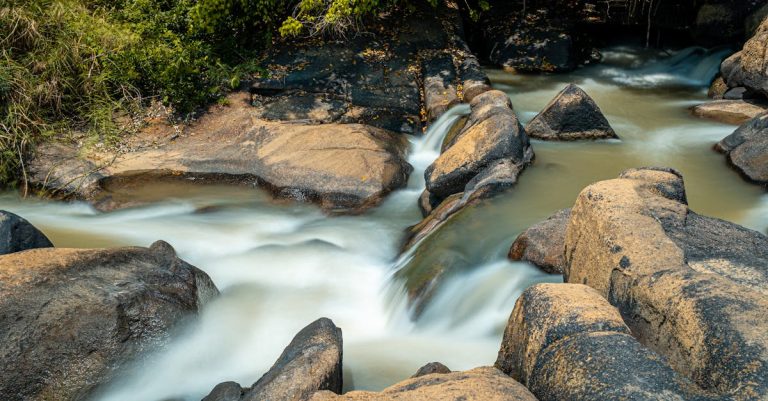 A tranquil waterfall flows over rocks in a lush green forest setting, showcasing nature's beauty.